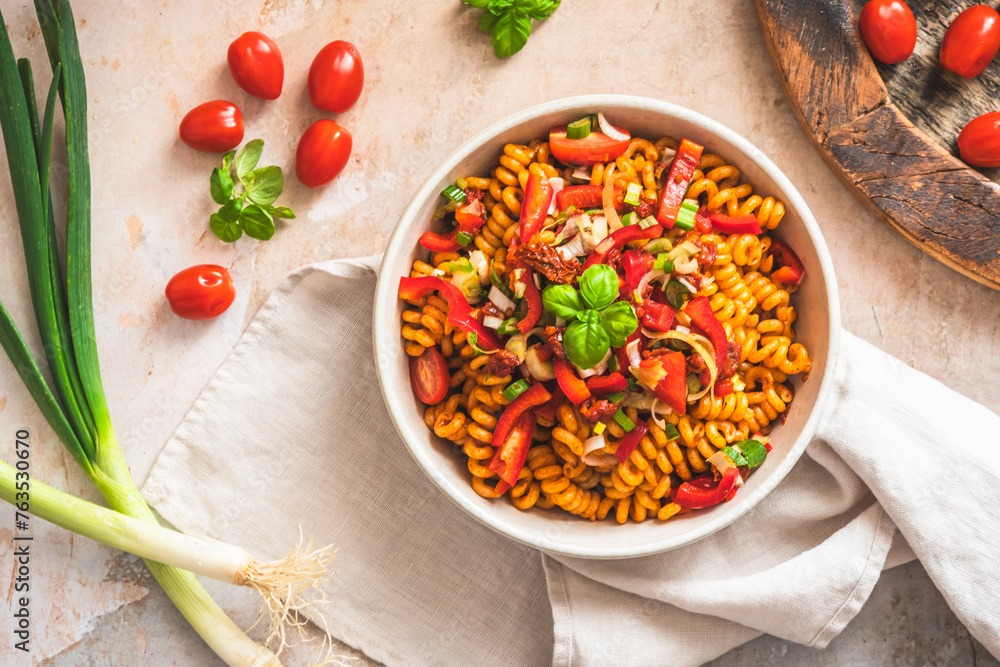 Pasta salad with pepper, tomatoes, spring onions and basil in a white bowl on light background, top view Pasta salad with pepper, tomatoes, spring onions and basil in a white bowl on light background, top view