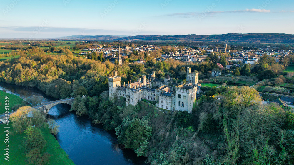 Aerial view of majestic Lismore Castle in County Waterford, Ireland, bathed in the golden glow of the setting sun on the first day of spring, showcasing its timeless beauty and historic charm