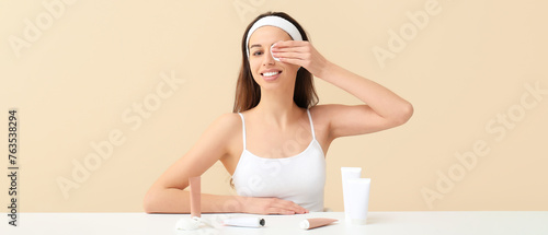 Beautiful young woman removing makeup with cotton pad on beige background