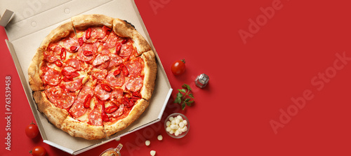 Delicious pepperoni pizza in cardboard box and ingredients on red background with space for text, top view © Pixel-Shot