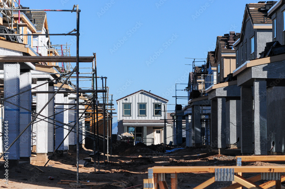 A two-story tract house under construction stands out at the end and the center of a new street, where two rows of similar houses are at different stages of development A two-story tract house under construction stands out at the end and the center of a new street, where two rows of similar houses are at different stages of development