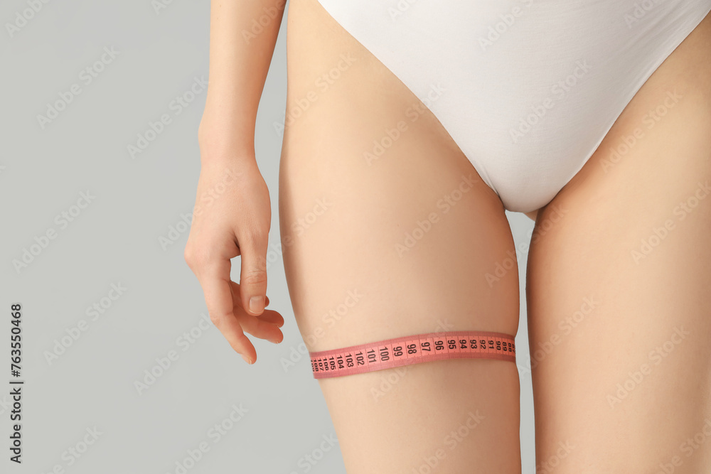Beautiful young woman in underwear with measuring tape on grey background. Concept of cellulite