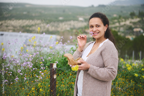 Charming woman collecting wildflowers, medicinal herbs and plants in mountains. People, nature and healthy lifestyle photo