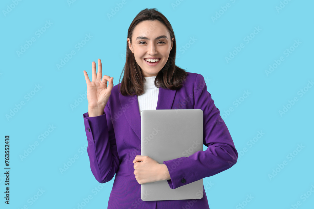 Young businesswoman with laptop showing OK gesture on blue background Young businesswoman with laptop showing OK gesture on blue background