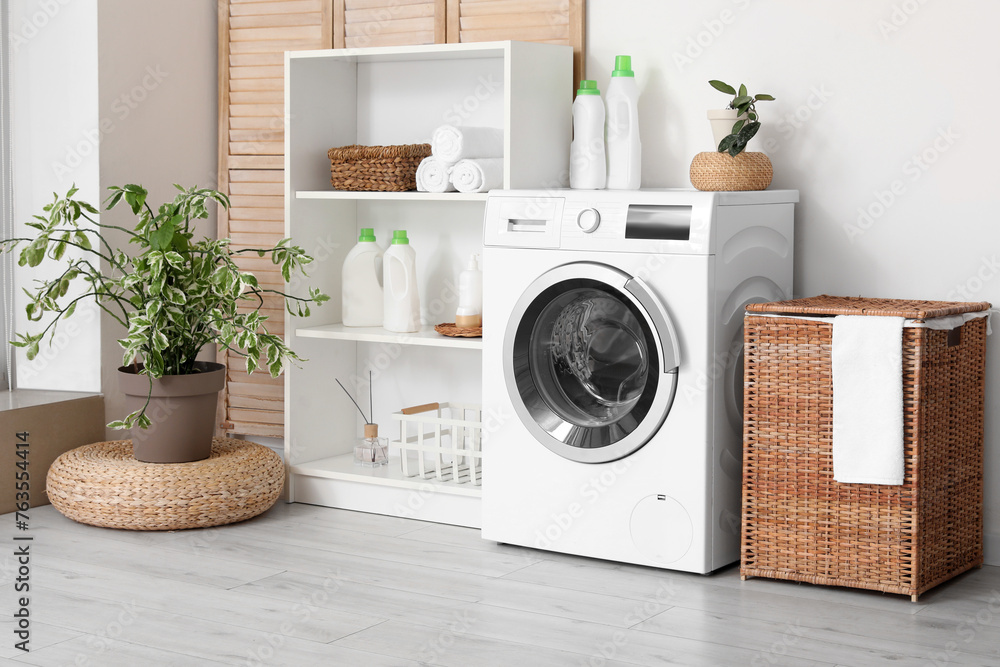 Modern washing machine with basket, shelving unit and dressing screen near white wall. Interior of home laundry room - obrazy, fototapety, plakaty 