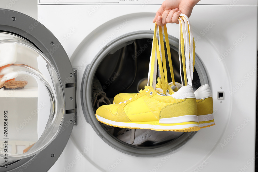 Female hands with sneakers and open washing machine, closeup Female hands with sneakers and open washing machine, closeup