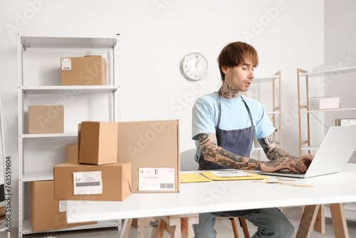 Young online store seller working with laptop at table in warehouse