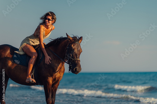 A happy lady is riding and petting a horse on a beach at sunset.