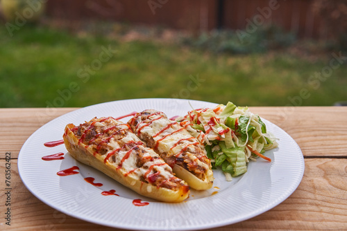 Traditional and healthy dish from east european or balkan cuisine, stuffed white pepper with minced pork, rice and cheese and served on white plate with vegetable salad outside in garden restaurant.