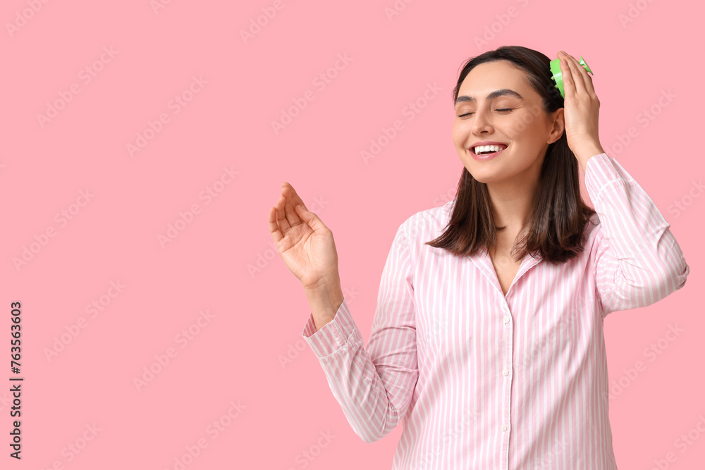 Obraz premium Beautiful young woman using hair scalp massager on pink background