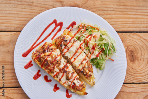 Yellow sweet paprika or peppers stuffed by minced pork meat and covered by sheep cheese and sprinkled by red chilli sauce on the white porcelain plate served with small lettuce salad as a side dish.