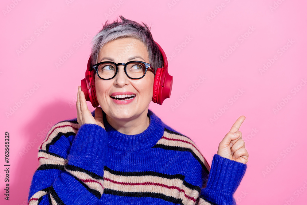 Photo portrait of lovely senior lady earphones point empty space dressed stylish blue striped garment isolated on pink color background