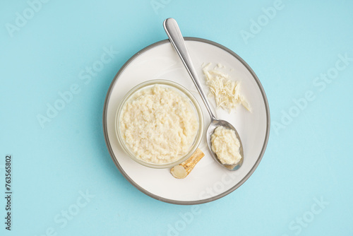 Foto Horseradish sauce in plate with bowl, spoon and ground horseradish root on blue background