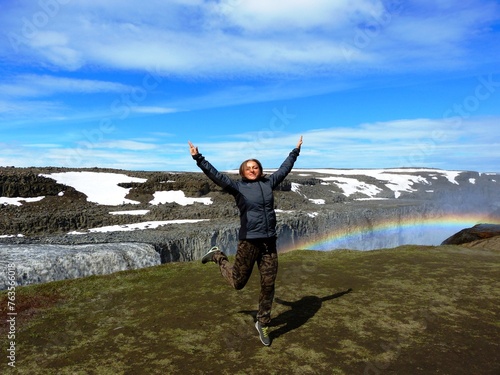 Happy woman tourist jumping in Iceland near waterfall Dettifoss.