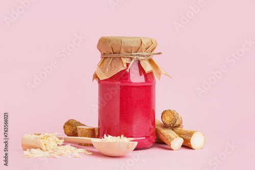 Horseradish sauce with beet in jar and spoon with ground horseradish on pink background