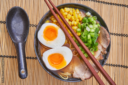 Close up picture on traditional japanese pork shoyu ramen soup in the rustic bowl with matching spoon and chopsticks on the bamboo mat. Delicious and tasty food, rich in the nutritions and flavour.