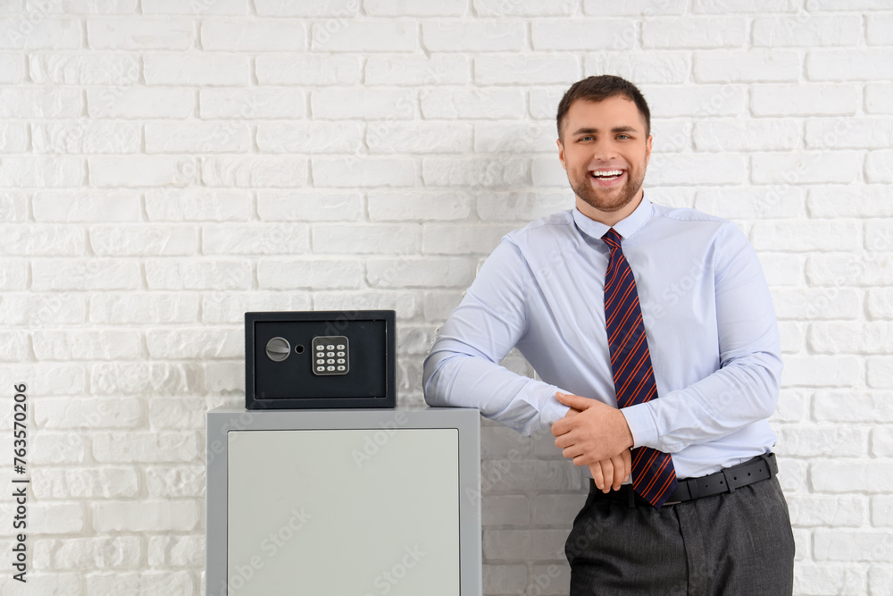 Happy young man with safe boxes on white brick background Happy young man with safe boxes on white brick background
