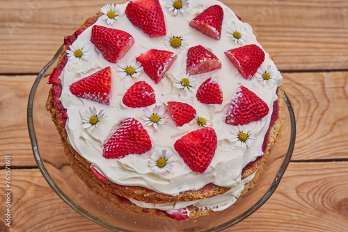 Top view on festive strawberry cake made from fresh strawberries, sour cream and mascarpone and decorated by fresh daisy flowers. The best cake for the young girl birthday celebration sweet and juicy.