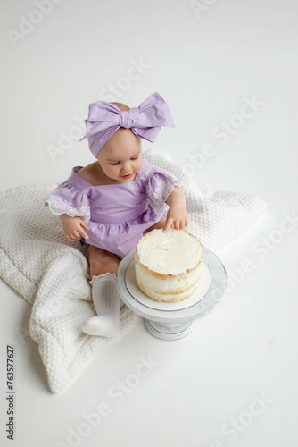 Cake crash. Photo session for baby's first birthday. Little elegant girl eats cake on a white background. Cyclorama.