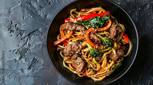 Stir-fried noodles with vegetables and beef served in a black bowl, against a slate background. Close-up shot captured from the top view.