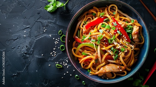 Udon stir-fry noodles with chicken meat and sesame served in a bowl, placed on a dark stone background with space for additional text or elements.