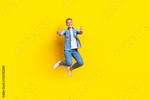 Full body photo of attractive young woman jumping show thumb up good quality wear trendy jeans clothes isolated on yellow color background © deagreez