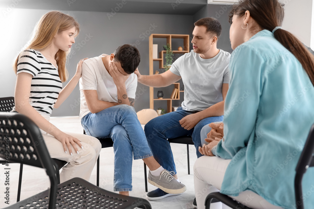 Young people calming sad man at group therapy session Young people calming sad man at group therapy session
