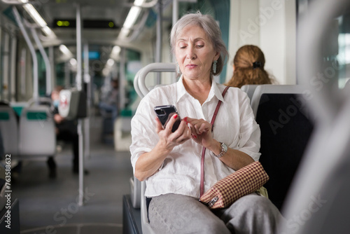 Gray haired caucasian woman sitting in tram and having telephone conversation.