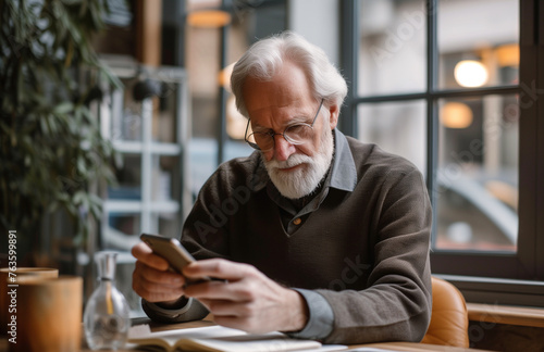 Elderly man using a smartphone, engrossed in modern technology in a home office setting.