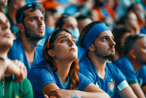 A group of male and female Italian football fans sit in the stadium with very sad faces and distressed expression and Hands clasped together desperately over her heads after losing the game  photo