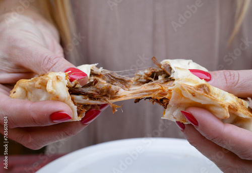 Eating empanadas. Closeup view of a woman hands breaking a flank steak meat and provolone cheese empanada.