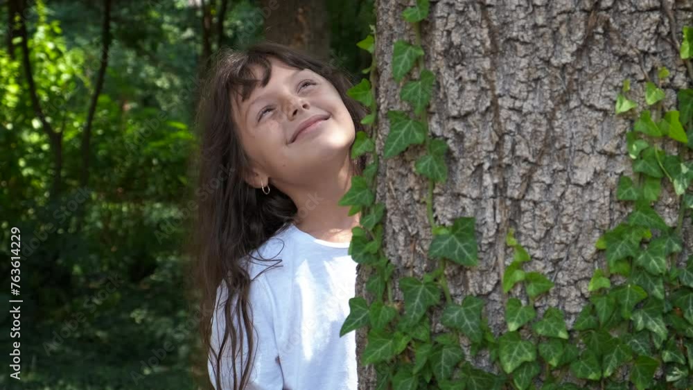 Alone child looking out from trunk in forest. An alone happy little girl look at the top of the green tree in the clean summer forest. Alone child looking out from trunk in forest. An alone happy little girl look at the top of the green tree in the clean summer forest.