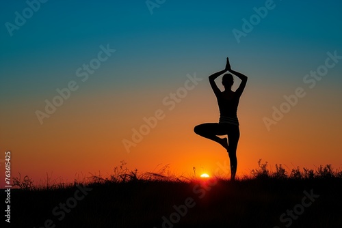 Female yoga practitioner holds a tree pose against the sunset in a field