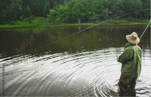 Man standing in a lake with waders on,  fly fishing. 