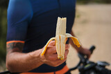 Man cyclist holding a banana with a background of a blue cycling jersey. Healthy nutrition of a cyclist. Healthy snack for a cyclist during training.