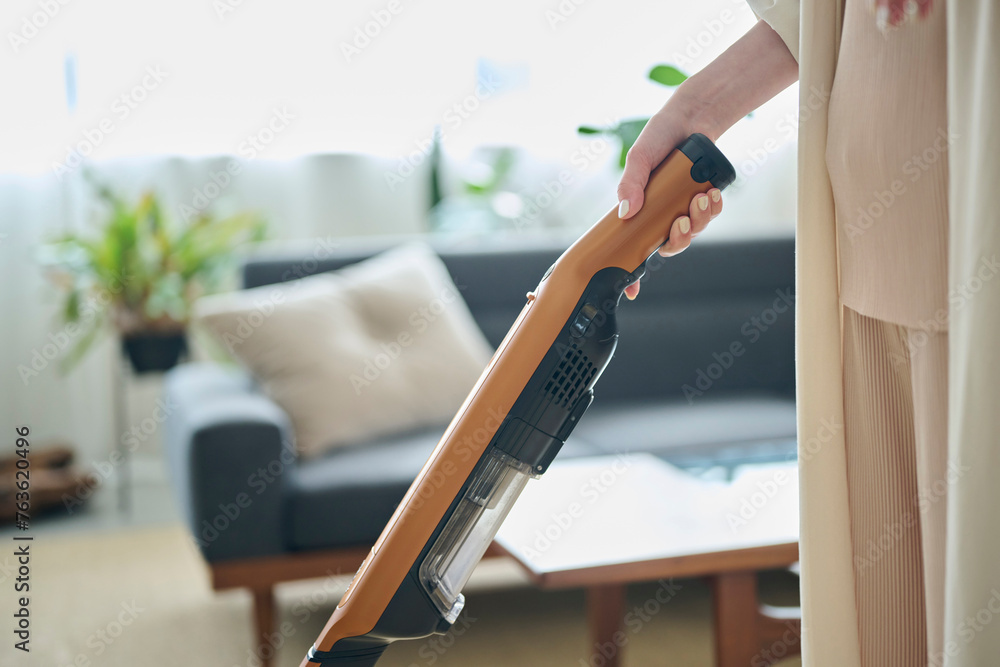 Obraz premium リビングで掃除機をかける20代女性