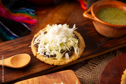 Sope. Traditional homemade Mexican food prepared with flattened and pinched on the border fried corn dough covered with refried beans, green or red sauce, lettuce, cheese, onion and sour cream.
