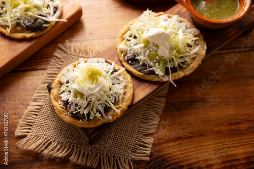 Sope. Traditional homemade Mexican food prepared with flattened and pinched on the border fried corn dough covered with refried beans, green or red sauce, lettuce, cheese, onion and sour cream.