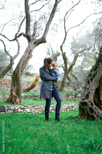 Mom with a little girl in her arms walks through a green park among the trees