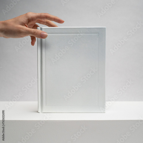 Female hands holding a blank notebook. Hardcover book. Matte white. Blank book mockup. Textured paper. (real photo) 3D render. Reaching out.  (ID: 763632698)
