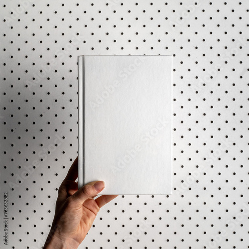 Male hand holding a blank notebook. Hardcover book. Matte white. Blank book mockup. Textured paper. (real photo) 3D render dots in background.  (ID: 763632822)