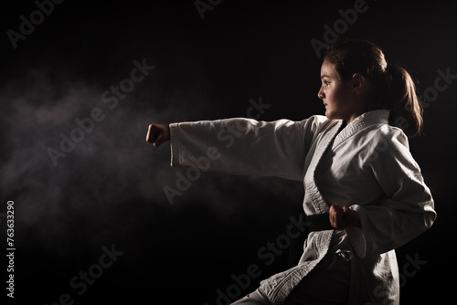 Young girl exercising karate. Child in kimono with smoke in the background.