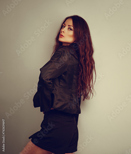 Sexy young beautiful woman with long brown hair posing in black fashion skirt and jacket on studio background. Closeup