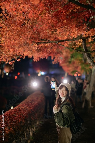 Asian woman in a stylish jacket enjoys the beauty of urban nightfall in Japan. A festive portrait capturing Christmas cheer amid the snowy landscape.