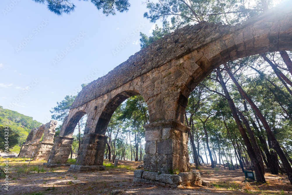View on summer sunny day of remnant of arched stone Roman aqueduct surrounded by green pines in Beydaglari Coastal National Park on site of ancient city of Phaselis in Kemer district, Turkey
