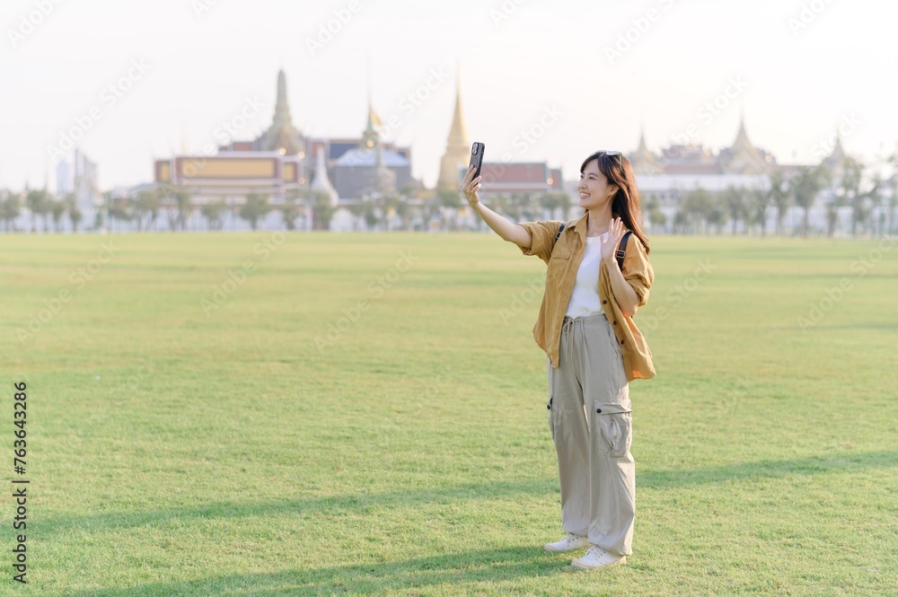 Traveler asian woman in her 30s take a livestream on smartphone while explores Wat Phra Kaew emerald Buddha. Share the wonders of Thai heritage through her journey.