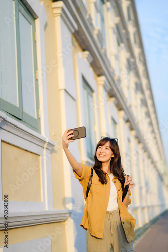 Traveler asian woman in her 30s making a livestream and sefie with a smartphone enjoying travel in Bangkok, Thailand. Journey trip lifestyle, world travel explorer or Asia summer tourism concept.