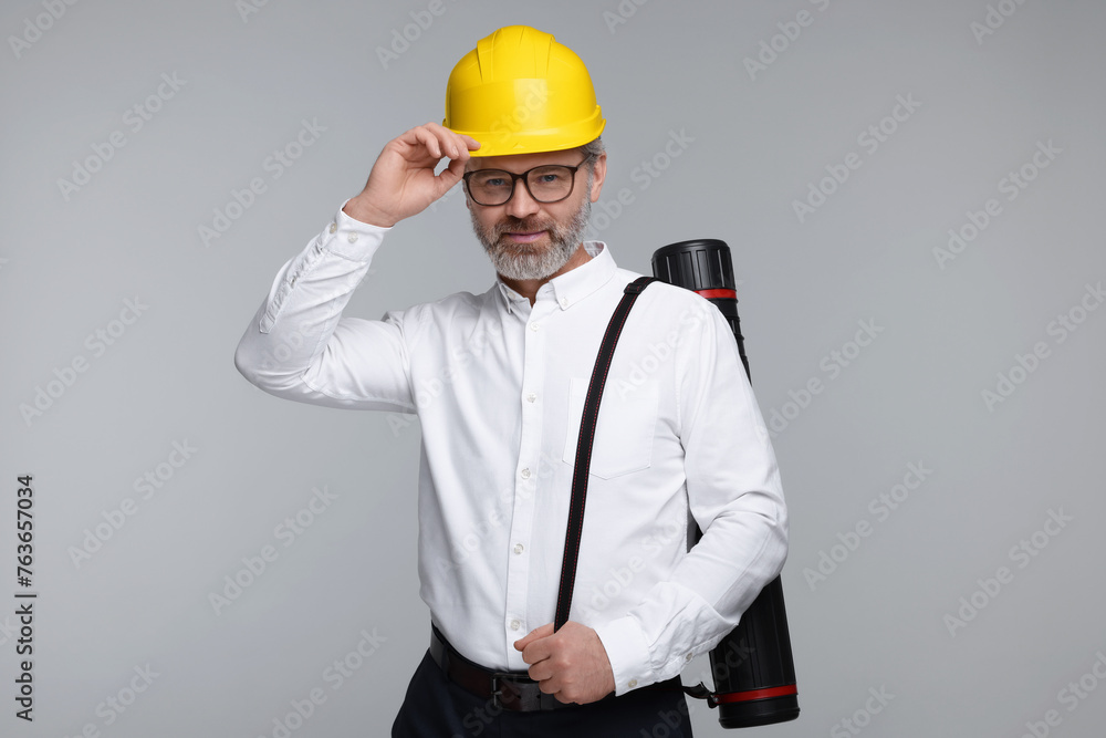 Architect in hard hat with drawing tube on grey background