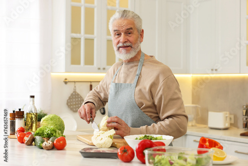Happy man cutting cauliflower at table in kitchen