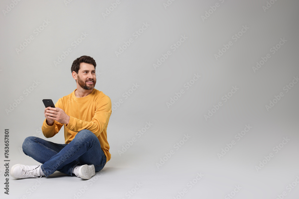 Smiling man with smartphone on grey background. Space for text Smiling man with smartphone on grey background. Space for text